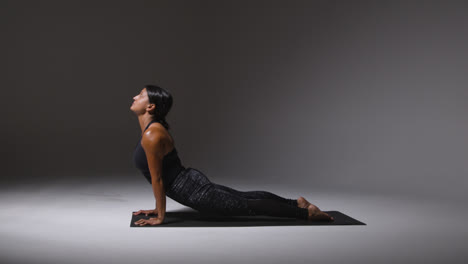 Studio-Shot-Of-Mature-Woman-Wearing-Gym-Fitness-Clothing-Standing-On-Mat-Doing-Variety-Of-Pilates-Stretching-Exercises-1